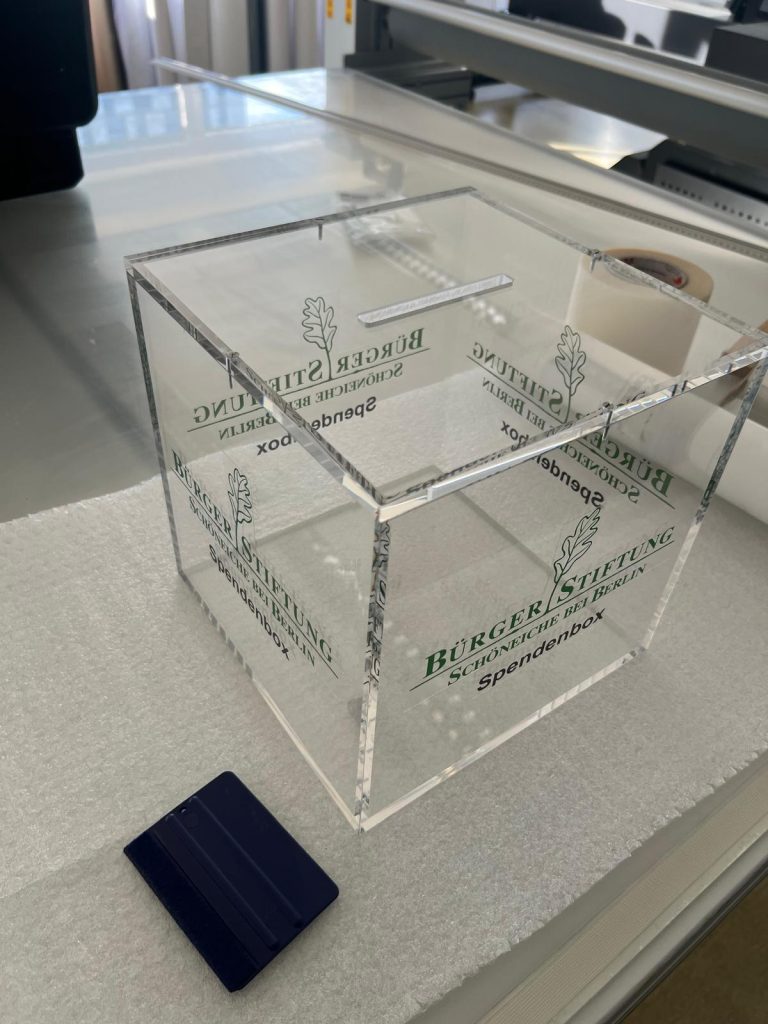 Spendenbox aus Acrylglas mit polierten Kanten und einem dezentem grünem Logo.