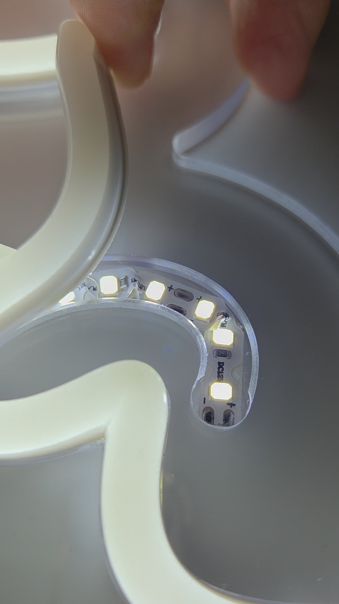 In einer Fräsnut liegt das LED-Band, welches im Bogen des Buchstabens gestaucht ist. Eine Hand hält das Silikonband nach oben. LED- und Silikonband gehören zum Produkt LED Flex Neon Generation 2 von Farben-Frikell | WTB.