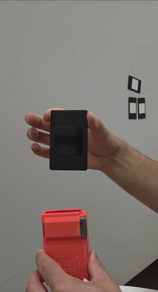 Sticky Cards um Folien zu positionieren mit zwei Seiten. Eine Hand zeigt das schwarze Gel-Pad für silikonisierte Trägerpapiere. Im Hintergrund kleben 3 Sticky Cards am Auto, bei denen das weiße Gel-Pad für Folien mit Papierträgern zu sehen ist.